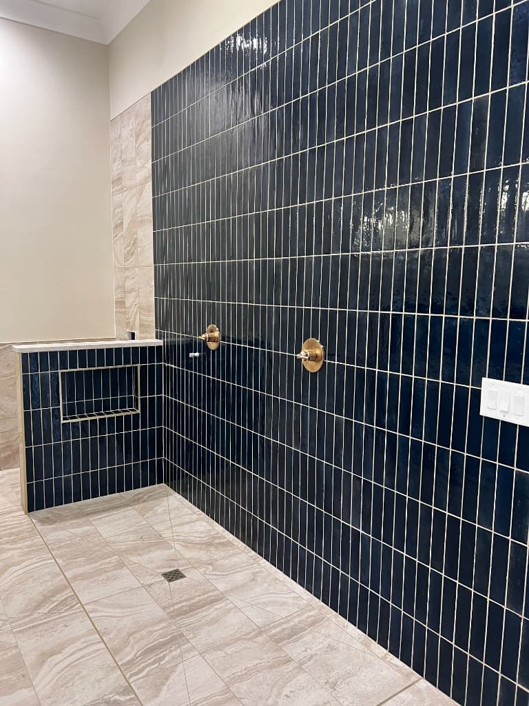 Navy vertical shower tile with brass fixtures and a stone niche, installed by AAnchor Ceramic Tile